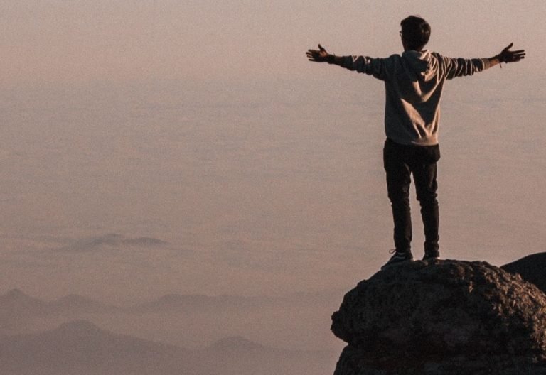 a man standing on top of a mountain with his arms outstretched.