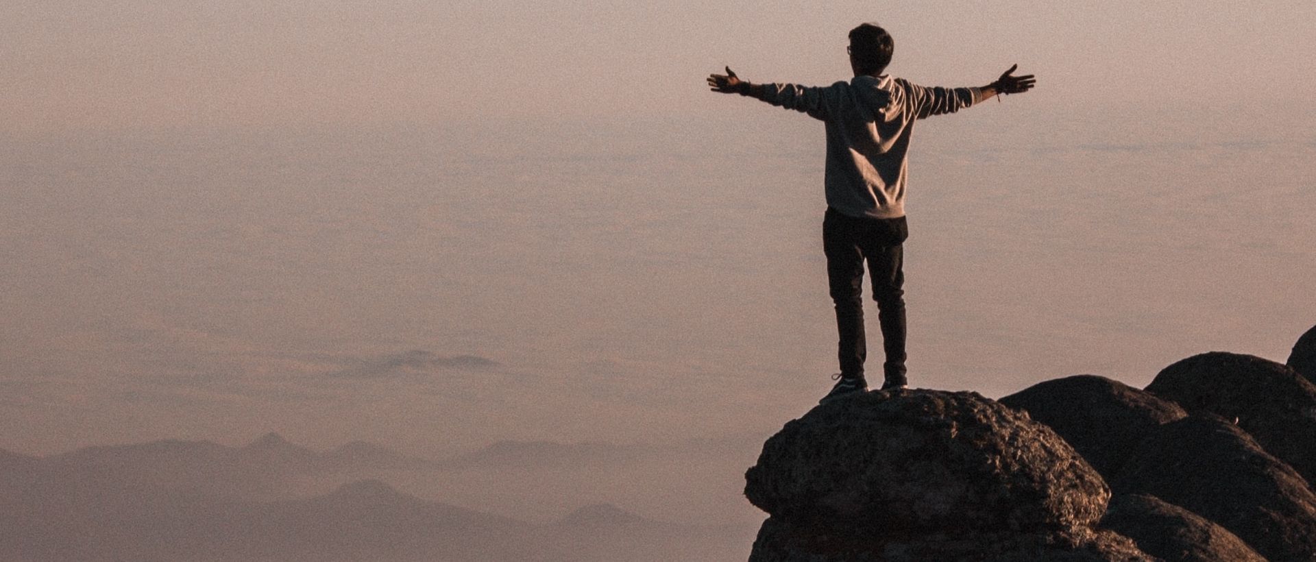 a man standing on top of a mountain with his arms outstretched.