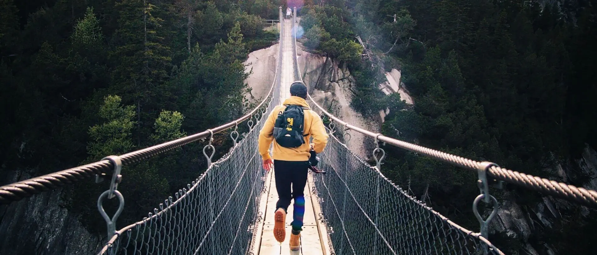 a man walking across a suspension bridge over a river.