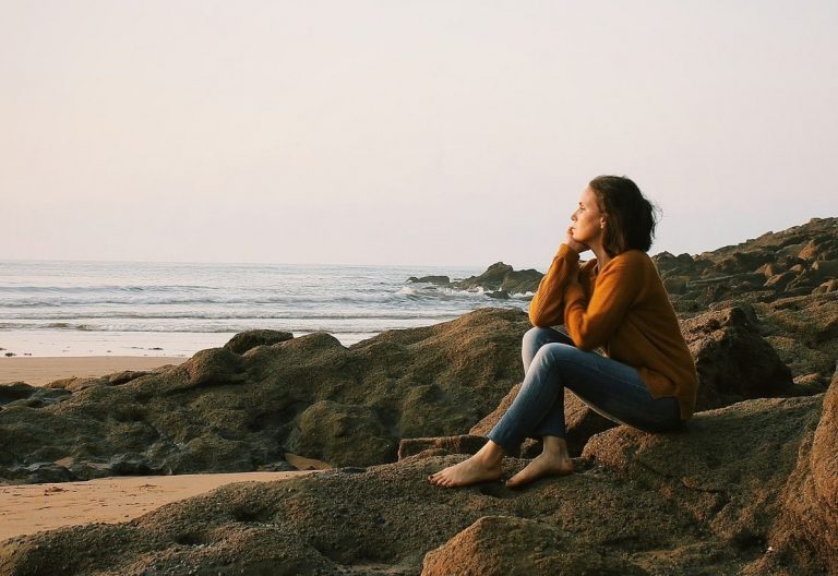 a woman sitting on a rock next to the ocean.