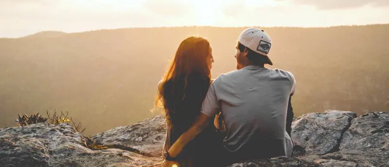 a man and a woman sitting on top of a mountain.