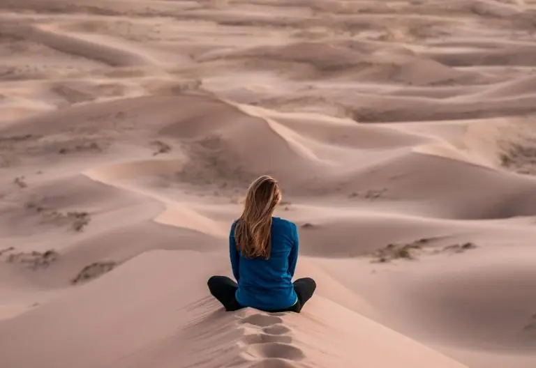 a woman sitting on top of a sand dune.