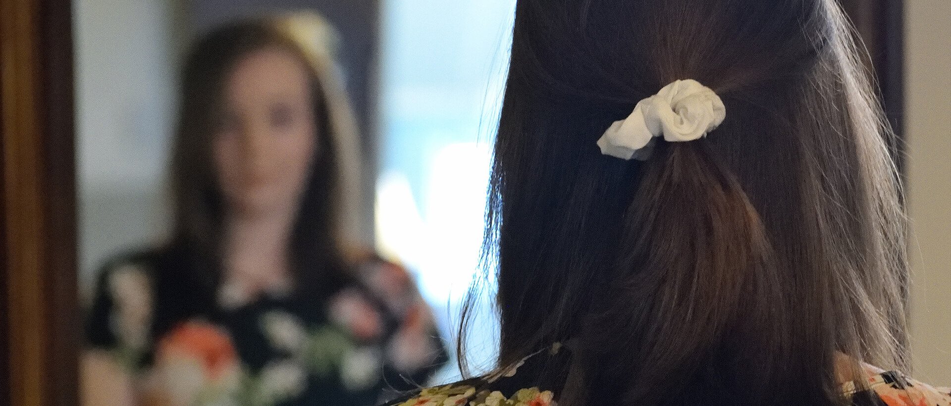 a woman standing in front of a mirror with a flower in her hair.