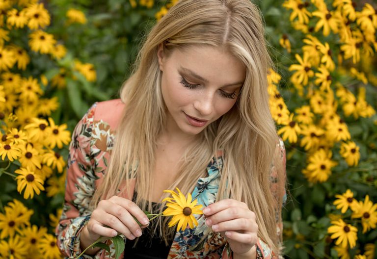 a woman holding a yellow flower in front of a bunch of yellow flowers.