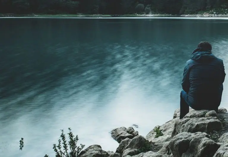 a person sitting on a rock looking at the water.