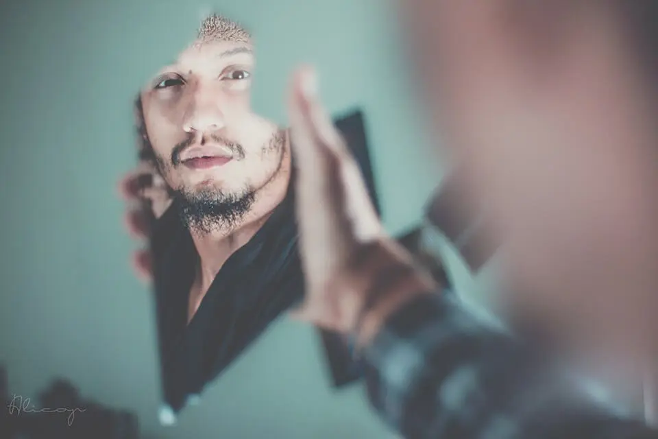 Man staring into his reflection, holding up a glass shard