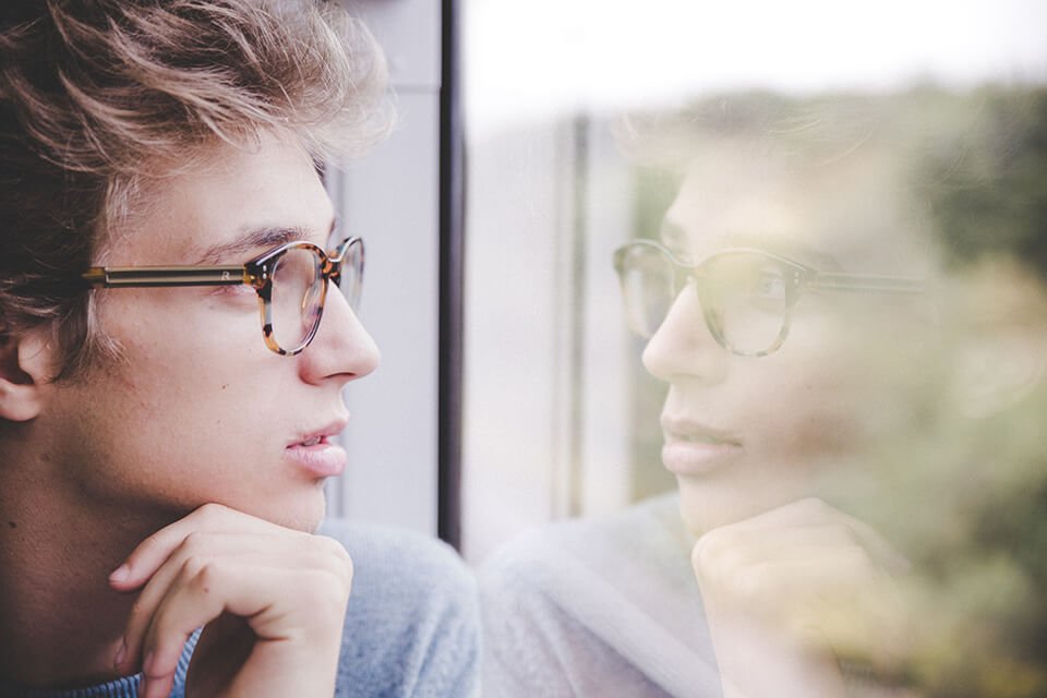 Man looking pensive into his reflection in the window