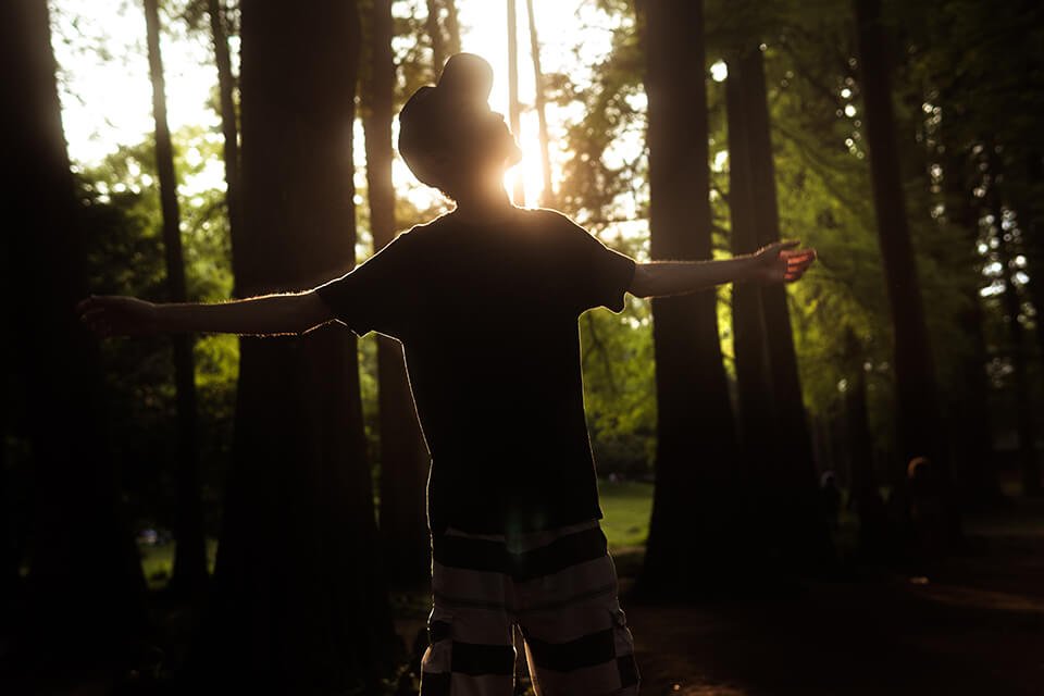 Man with his arms open, looking up in the middle of a forest