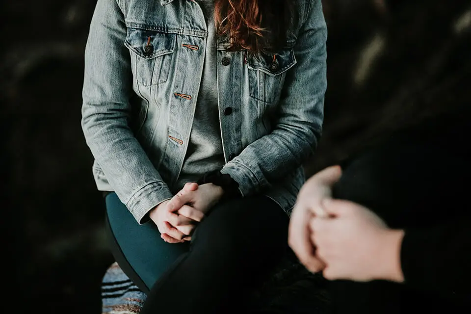 a woman in a jean jacket sitting on a bench.