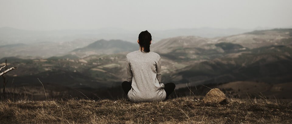 a woman sitting on top of a grass covered hillside.