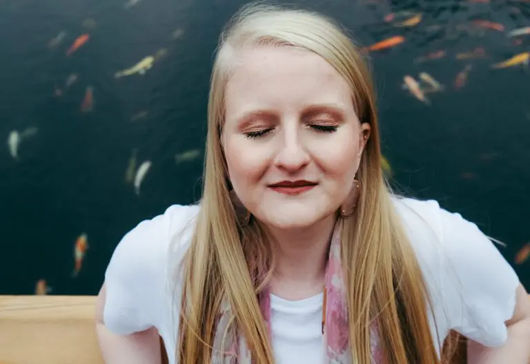 a woman with long blonde hair sitting in front of a pond.