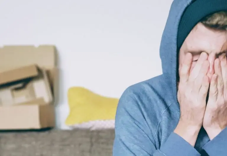 a man sitting on a couch covering his face with his hands.