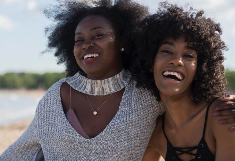 a couple of women standing next to each other on a beach.