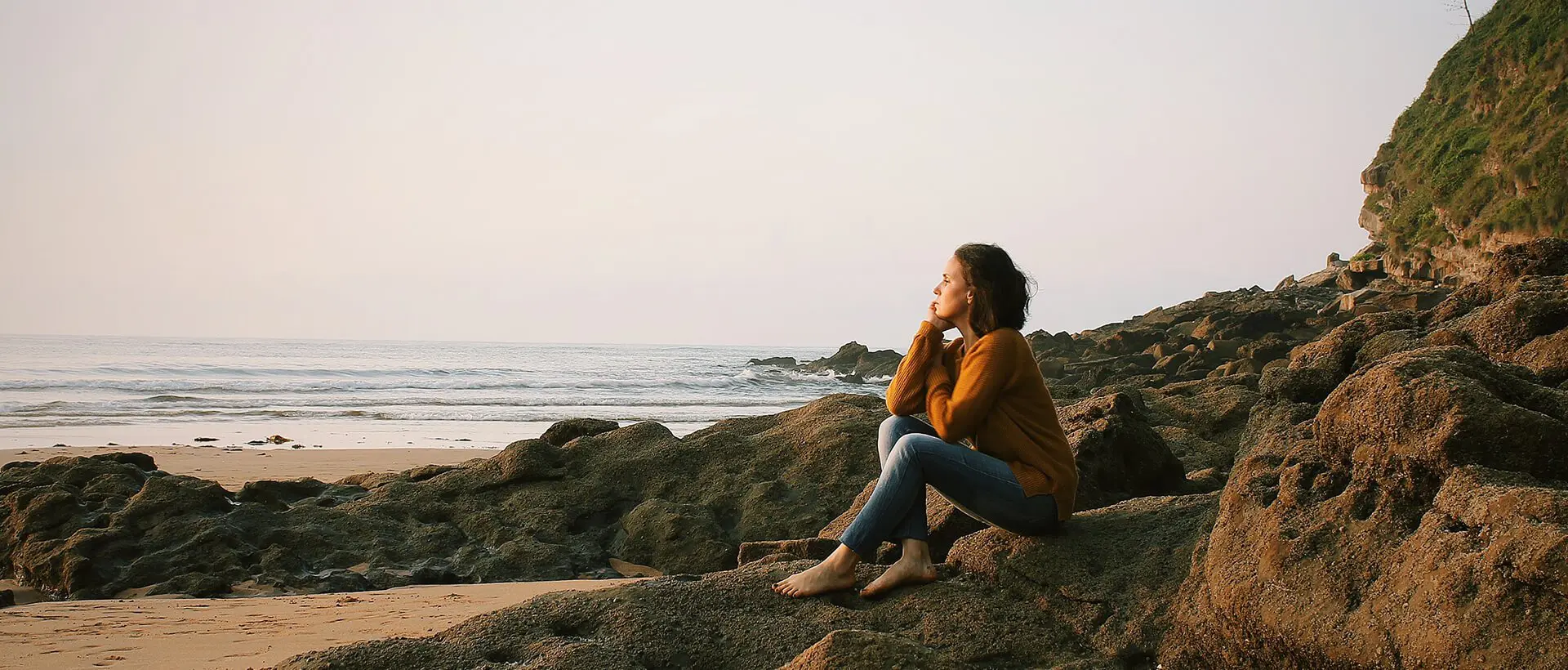 a woman sitting on a rock next to the ocean.