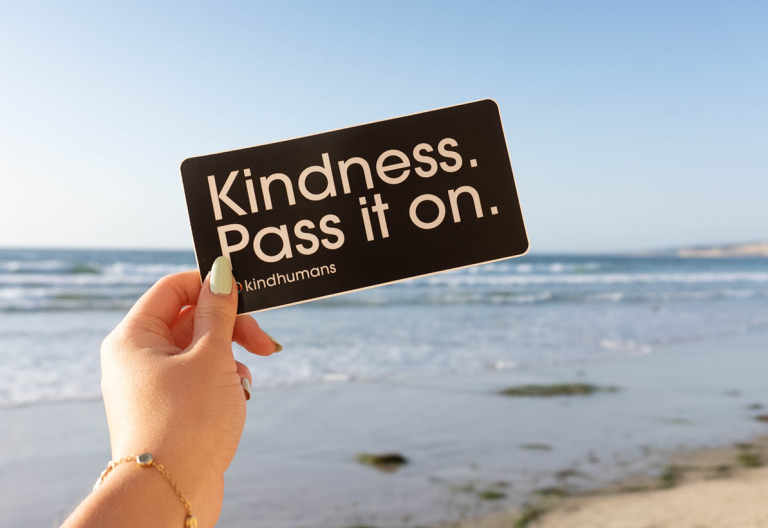 a person holding up a sign that says kindness pass it on.