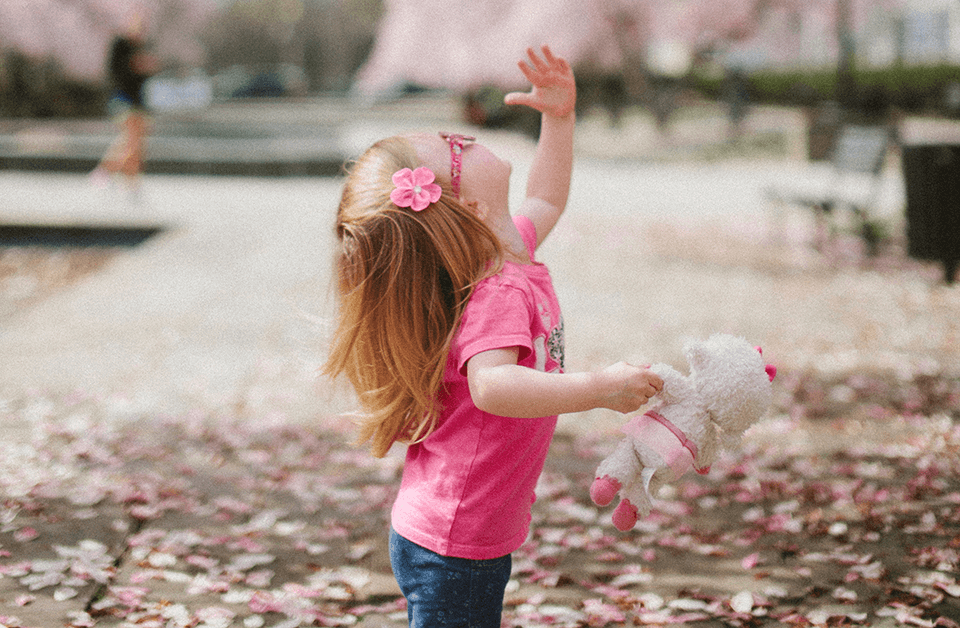 Little girl looking up at tree holding her toy