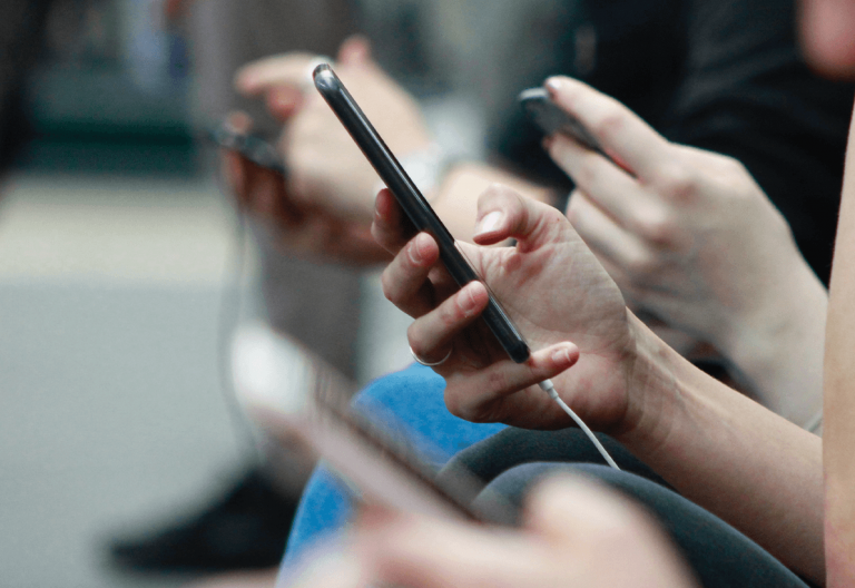 a group of people sitting next to each other using cell phones.